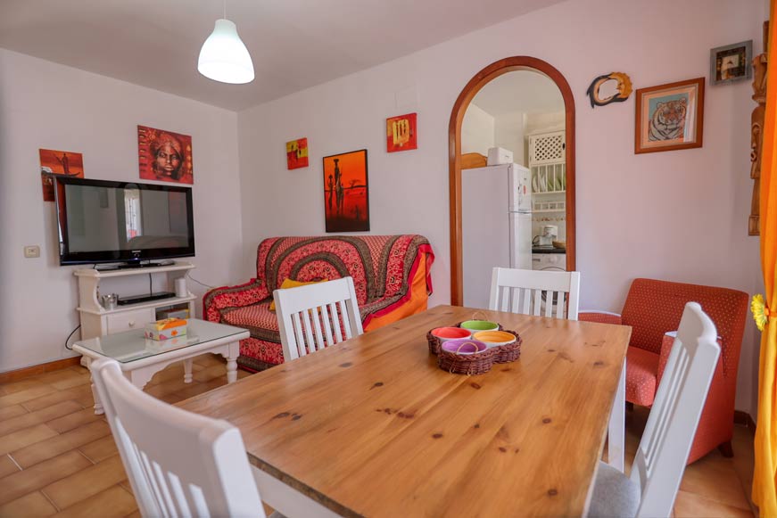 Mesa de comedor de madera junto a salón decorado y televisión visible