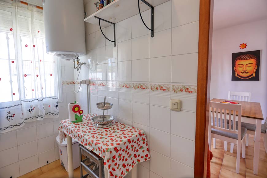Cocina pequeña con mesa auxiliar y vista al comedor desde la puerta