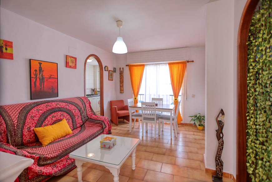 Salón con sofá, mesa blanca y cortinas naranjas junto a comedor