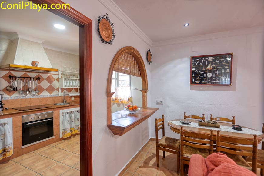 Vista desde el comedor hacia una cocina con pasaplatos y mesa de madera