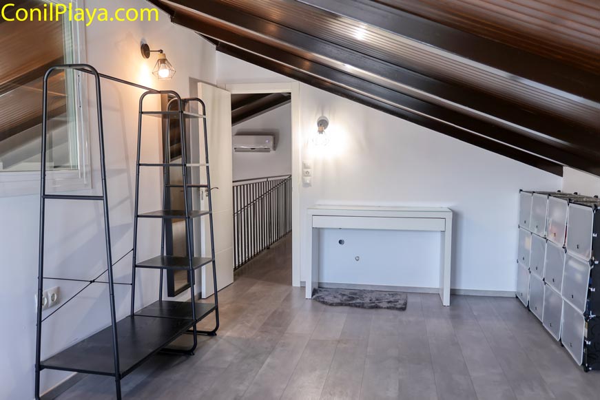 Dormitorio abuhardillado con armario estantería y mesa blanca bajo techo inclinado