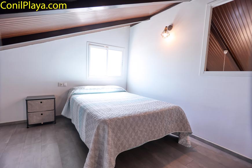 Dormitorio abuhardillado con cama doble cerca de una ventana y mesita