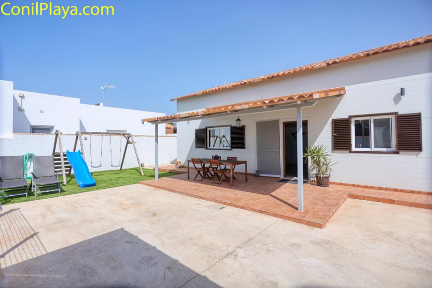 Porche con mesa de jardín y zona infantil visible al fondo