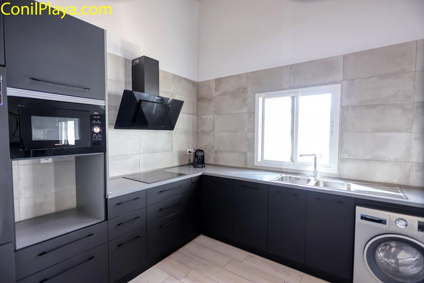 Cocina moderna con muebles oscuros, electrodomésticos y ventana grande al fondo