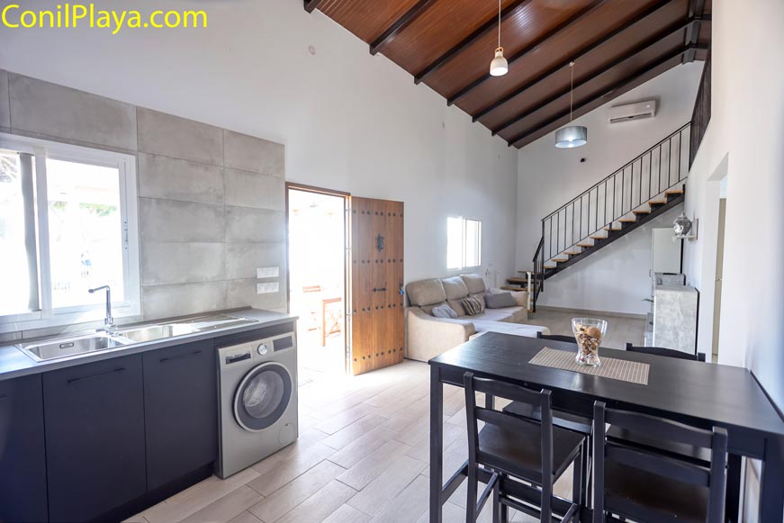 Salón moderno con sofá, mesa comedor y cocina abierta bajo techo de madera