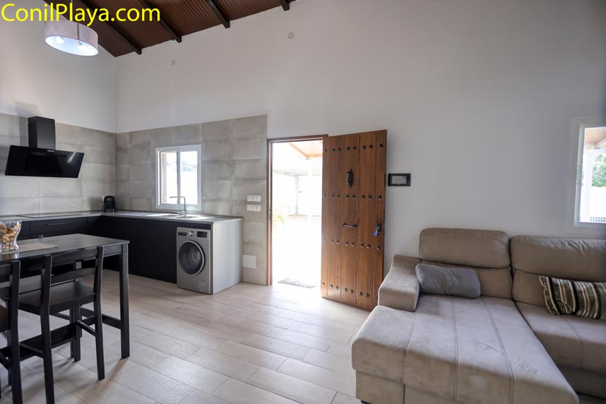 Salón con sofá y cocina integrada junto a puerta de madera
