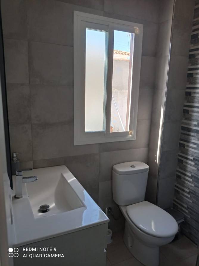 Cuarto de baño pequeño con lavabo, ventana y paredes de azulejo gris