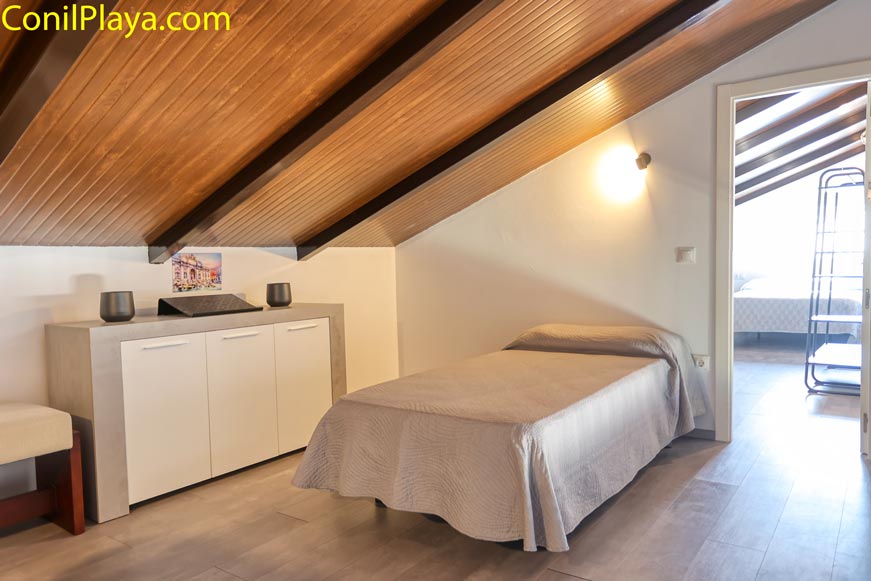 Dormitorio abuhardillado con cama individual y techo de madera visible