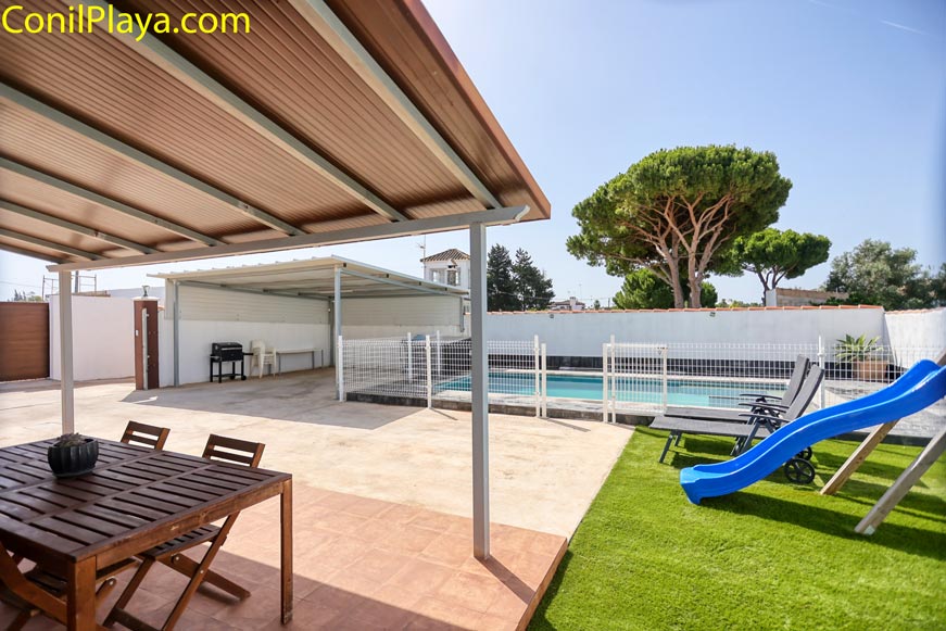 Vista de piscina vallada junto a porche cubierto y zona de juegos infantiles