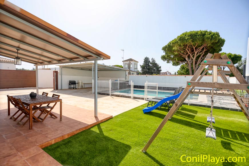 Porche con mesa de jardín, piscina vallada y columpio infantil en zona exterior