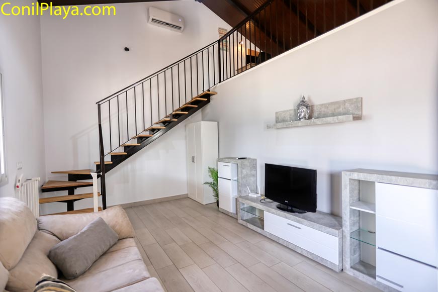 Salón moderno con sofá, televisor y escalera de madera vista desde la puerta