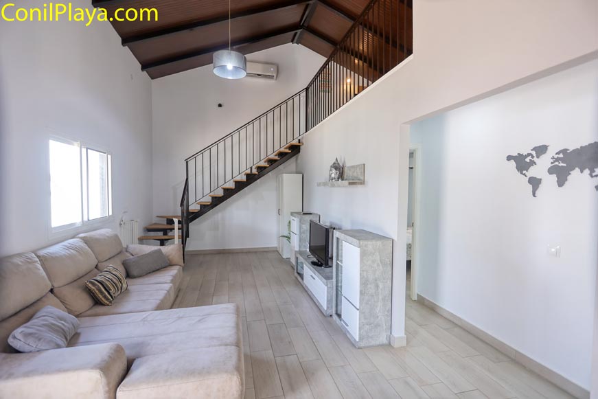 Salón moderno con sofá grande y escaleras de madera vistas desde la entrada