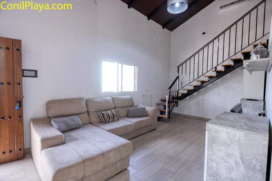 Salón con sofá chaise longue y escalera moderna vista desde la entrada