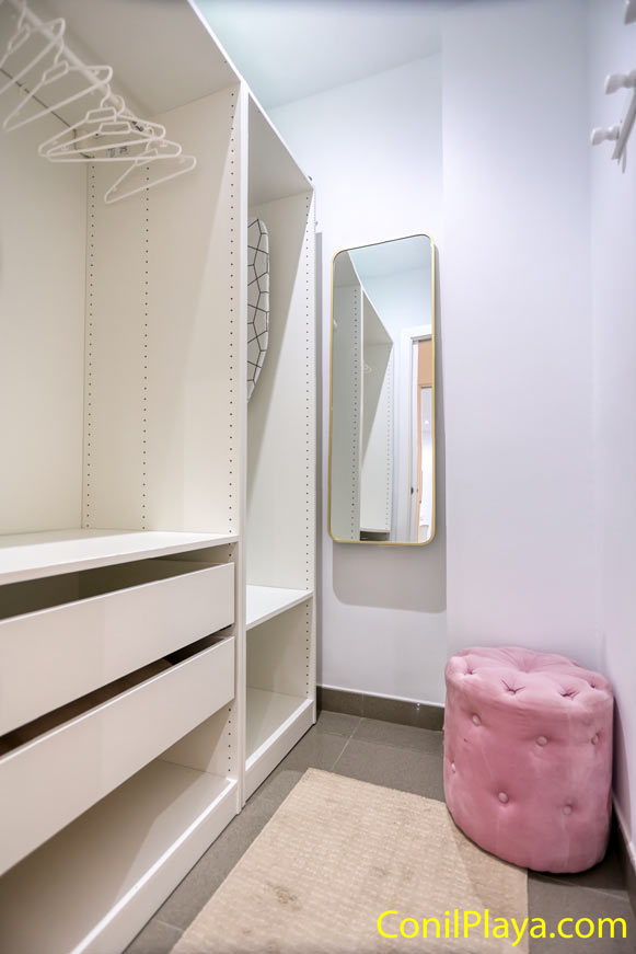 Vestidor interior con espejo y asiento rosa junto a armario blanco abierto