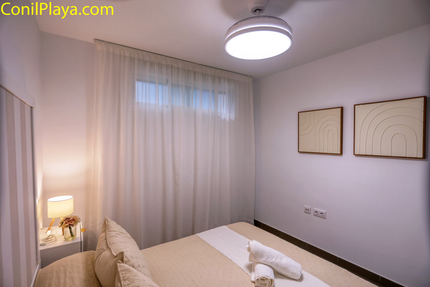 Dormitorio moderno con cama doble, cuadros decorativos, luz cálida suave y ventilador de techo