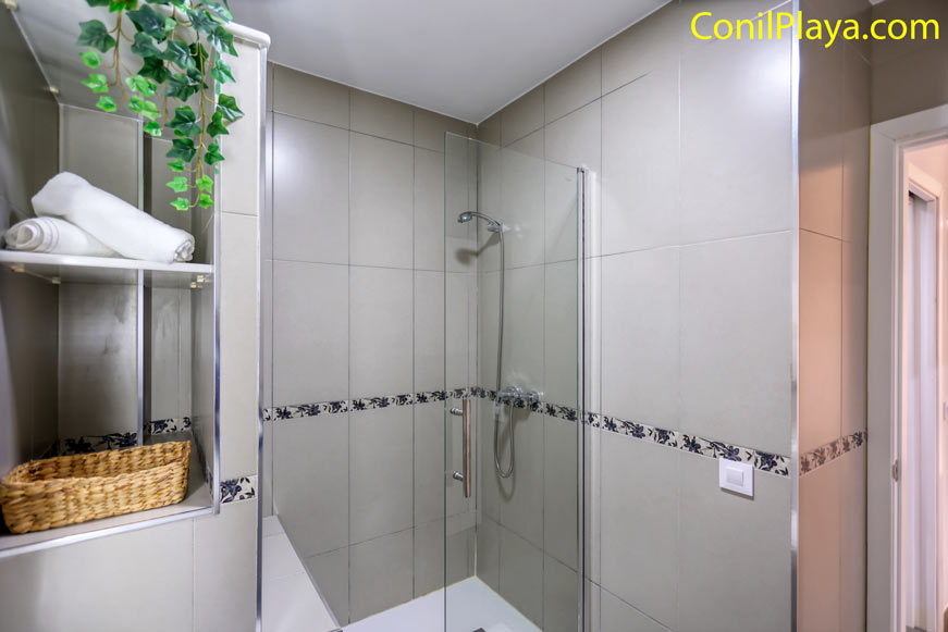 Cuarto de baño con ducha acristalada y estantería con toallas y cesta