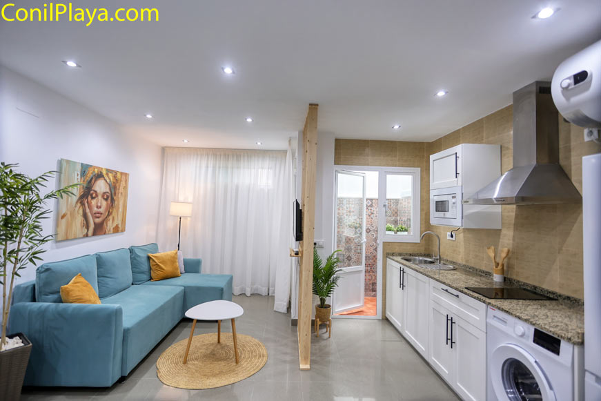 Salón con sofá azul amplio y cómodo, mesa redonda y cocina integrada al fondo