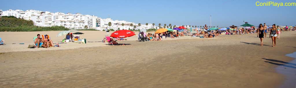 playa de los bateles con conil al fondo y gente paseando por la playa