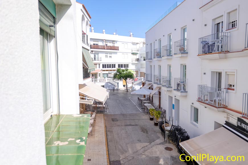 Vista desde de la ventana de la cocina hacia calle peatonal con terrazas y edificios blancos