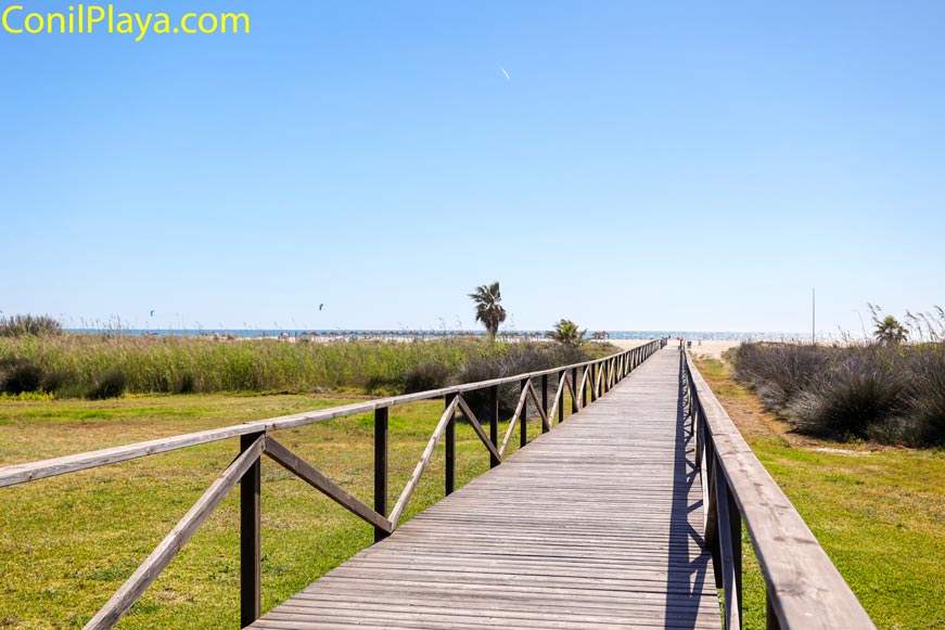 Pasarela de madera sobre césped que conduce hacia la playa de los bateles