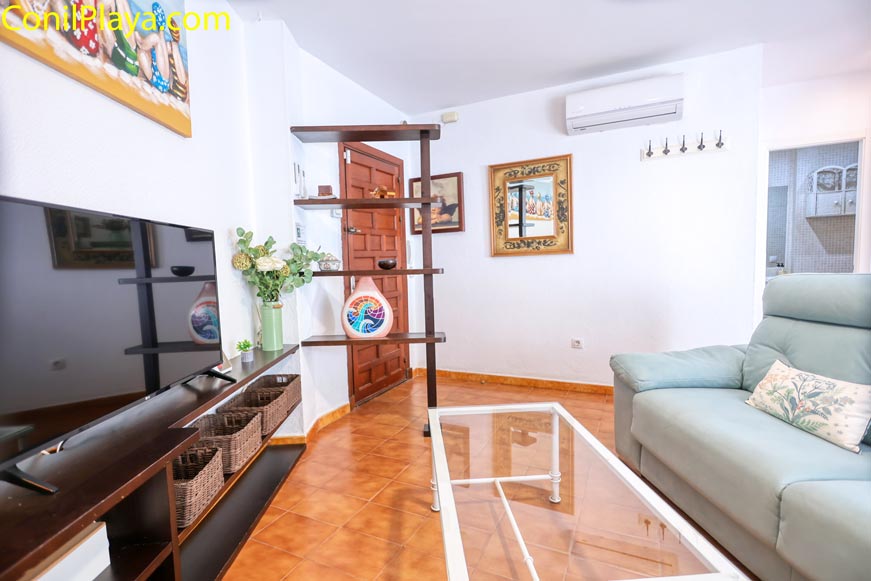 Salón amueblado con sofá, televisión y mesa de cristal desde el recibidor