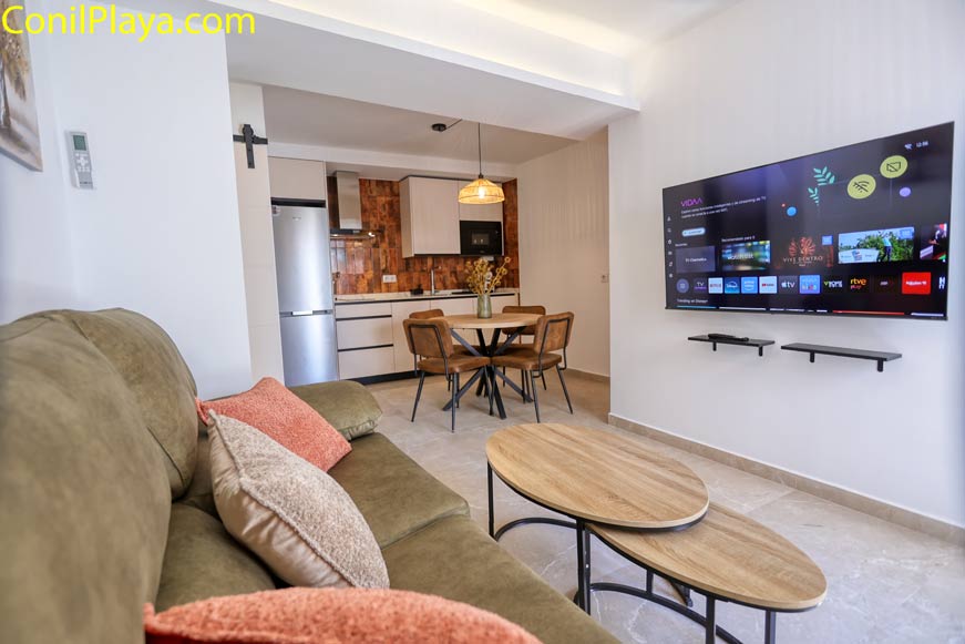 Salón moderno con sofá verde, televisión grande y mesa de centro ovalada