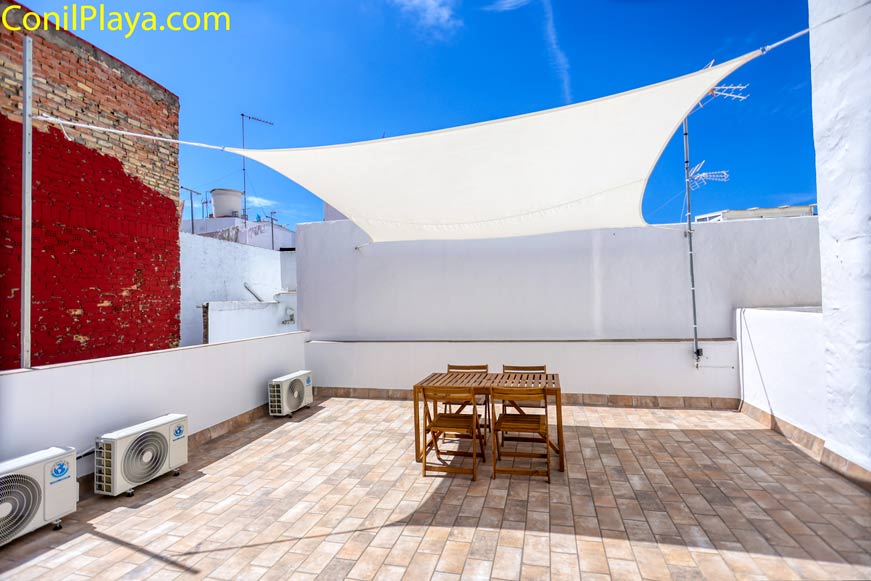 Terraza amplia con mesa y sillas de madera y toldo de sombra