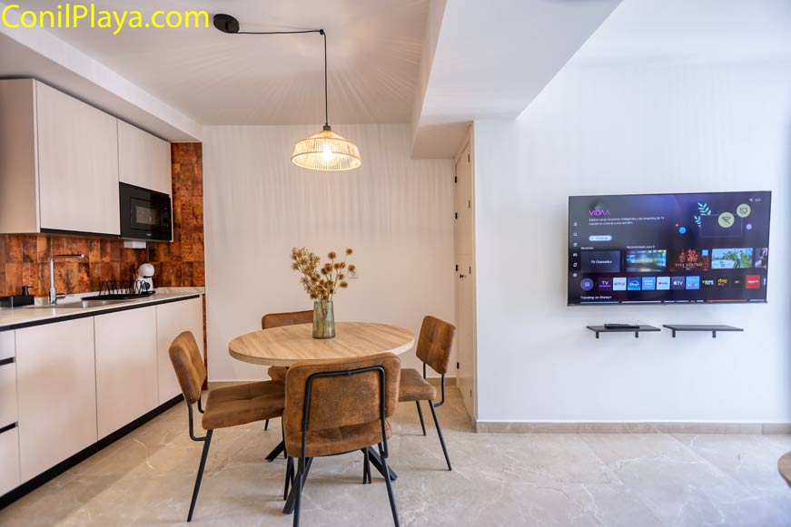 Cocina moderna con mesa redonda, sillas marrones y televisión en la pared