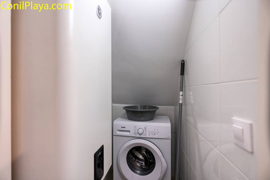 Espacio pequeño con termo eléctrico, lavadora debajo de escalera y fregona a un lado