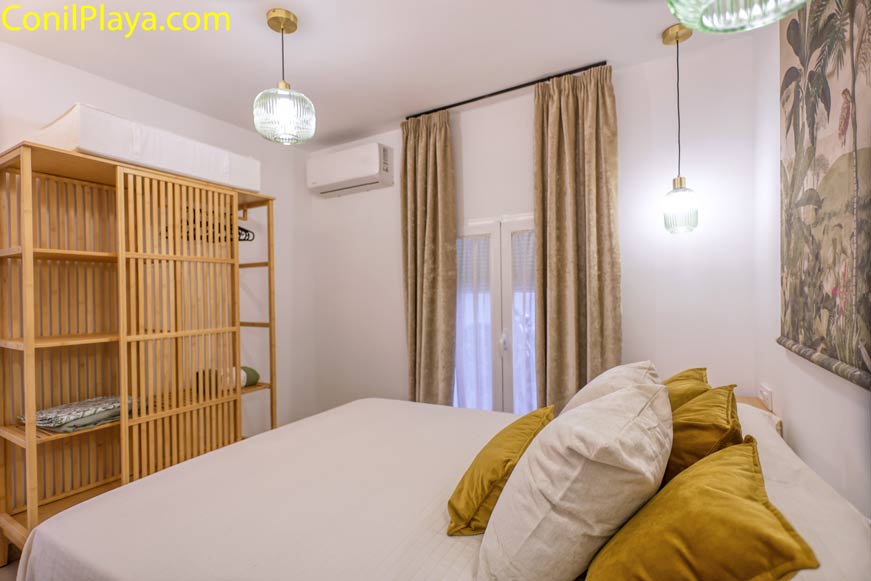 Dormitorio principal con armario de madera, aire acondicionado y cama con cojines amarillos