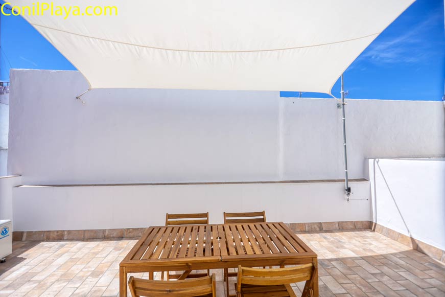 Terraza amueblada con mesa y sillas de madera bajo toldo en la azotea