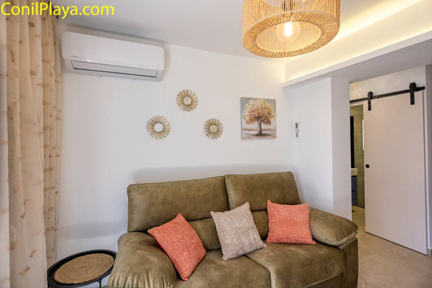 Salón moderno con sofá verde cojines puerta corredera y aire acondicionado