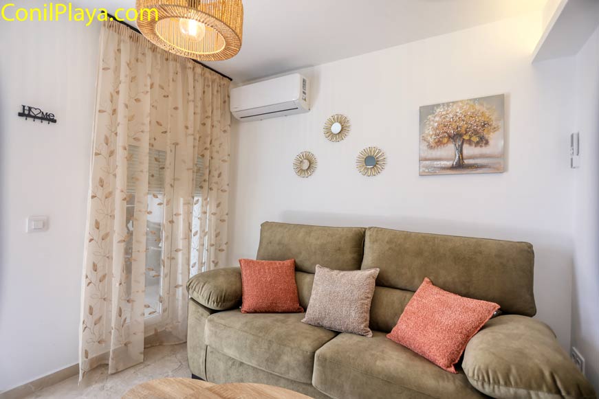 Sofá con cojines y decoración en pared cerca de ventana con cortinas