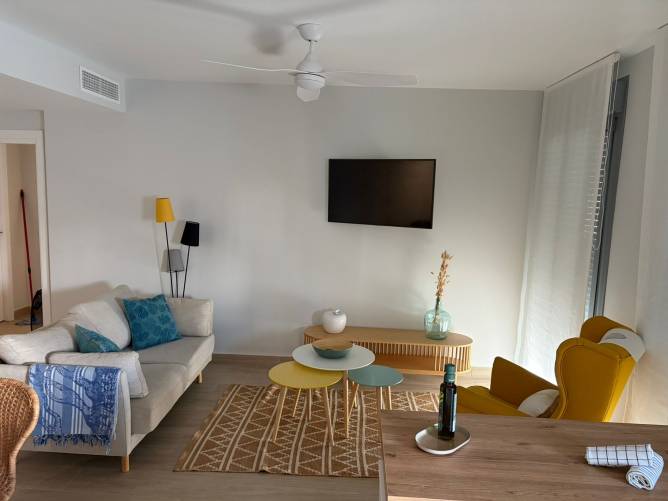 Vista frontal del salón con ventilador de techo, alfombra geométrica y mobiliario nórdico