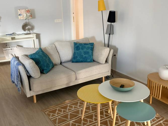 Sofá beige con cojines turquesas y mesas auxiliares de colores en salón de Conil