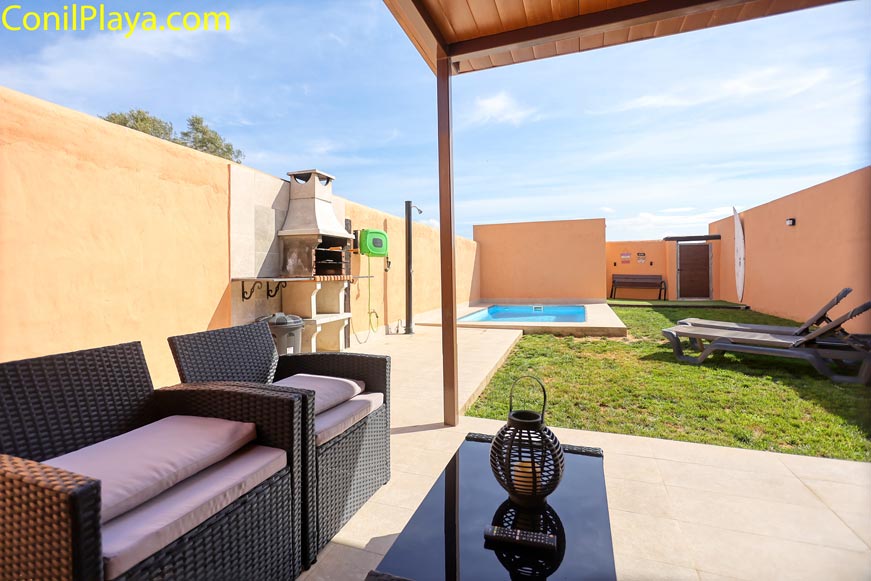 Zona exterior con sofá barbacoa piscina y tumbonas vista desde el porche