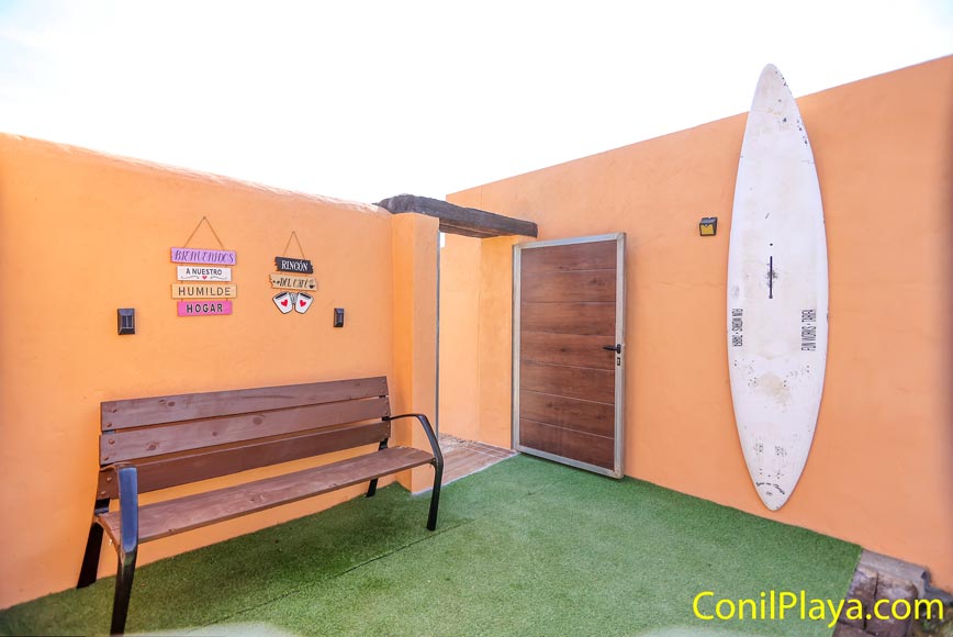 Pequeño porche con banco de madera y tabla de surf junto a la puerta