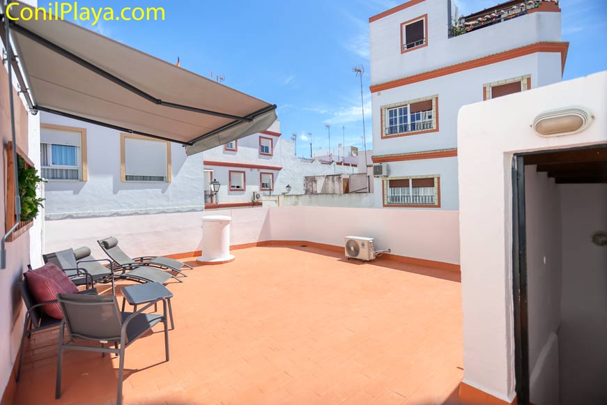 Amplia terraza con varias tumbonas y toldo junto a edificios vecinos