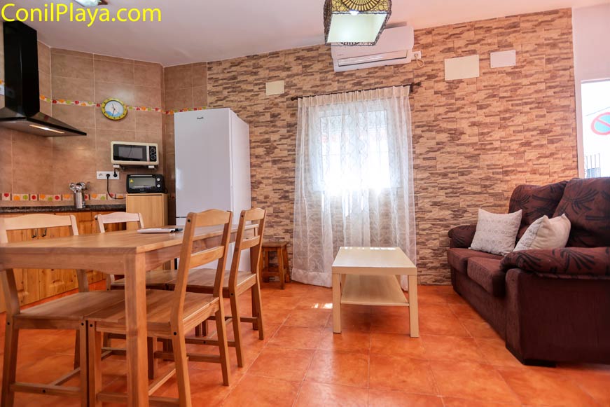 Salón con mesa de comedor, sofá marrón y cocina abierta al fondo