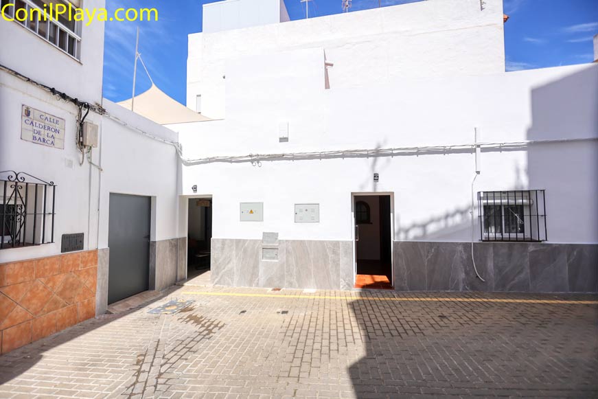 Fachada blanca moderna con ventanas enrejadas, dos puertas abiertas y calle adoquinada bajo cielo azul despejado.