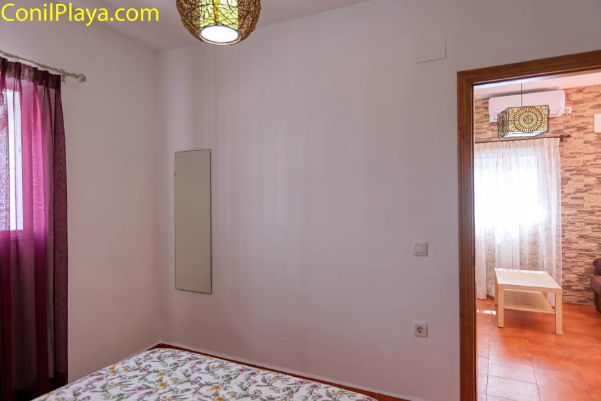 Dormitorio con espejo en la pared, cortina morada y puerta hacia salón con aire acondicionado