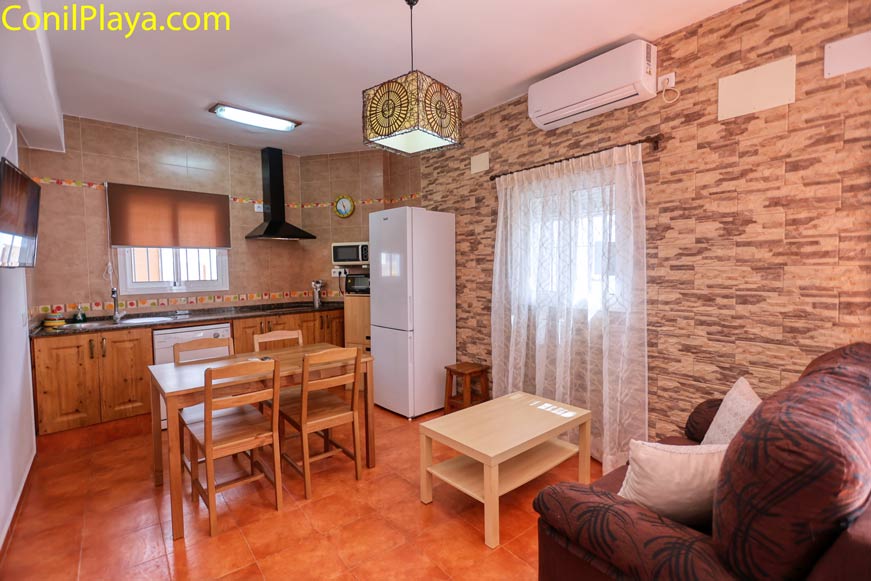 Cocina abierta con muebles de madera, comedor y sofá vistos desde la entrada