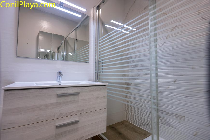 Mueble de baño blanco junto a ducha con mampara de cristal moderna