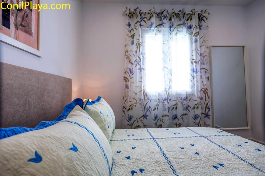 Dormitorio con ventana, cama y espejo en una esquina