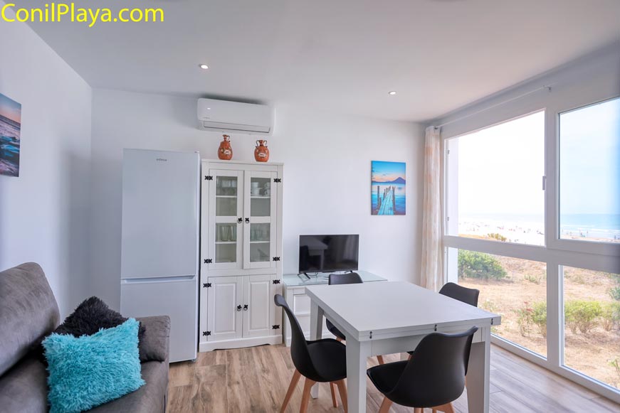 Salón con sofá gris, mesa blanca y grandes ventanales al exterior