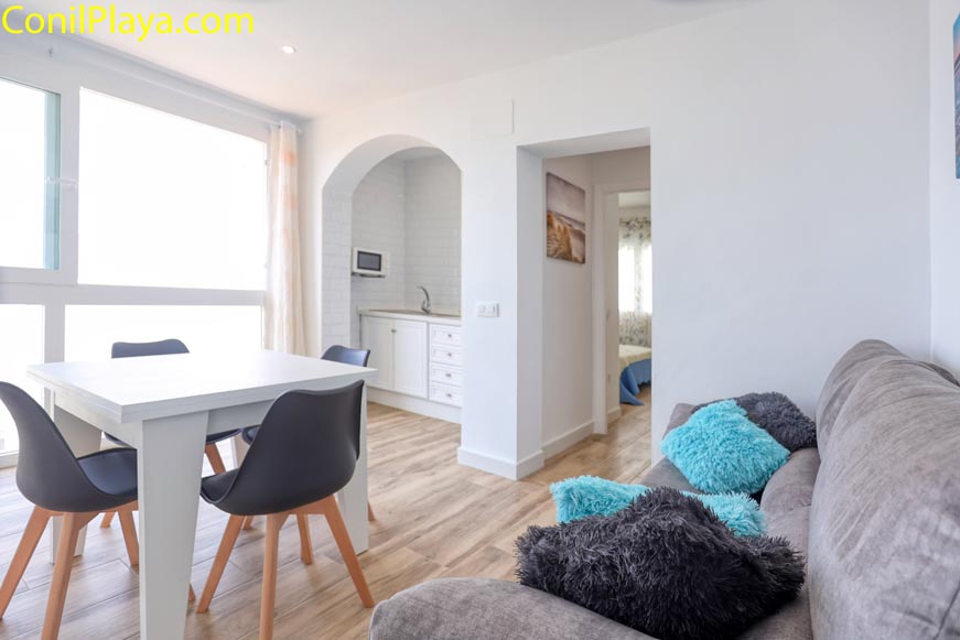 Salón con sofá gris, mesa blanca y acceso a cocina