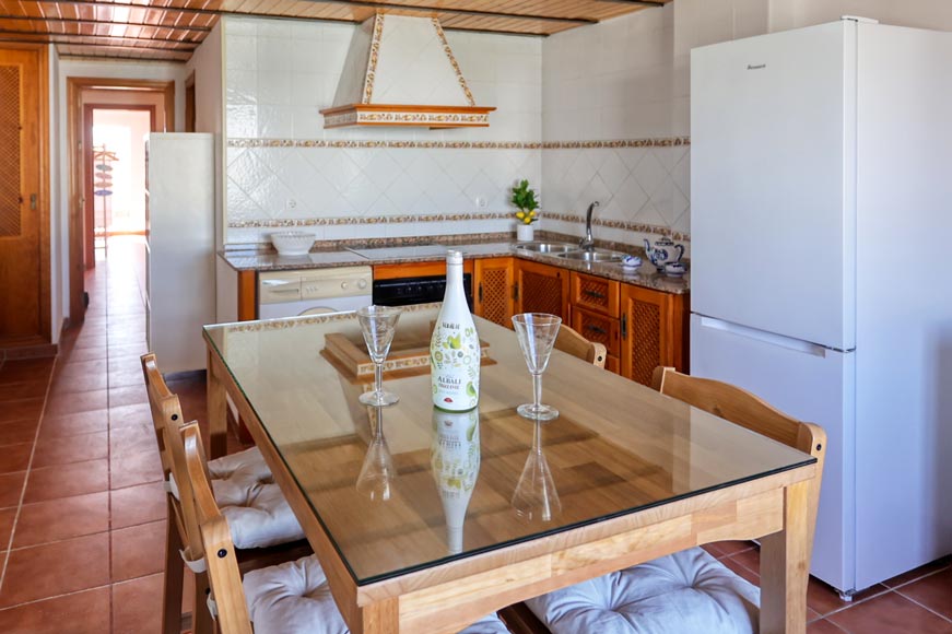 Mesa alta con la cocina al fondo, frigorífico y muebles de madera