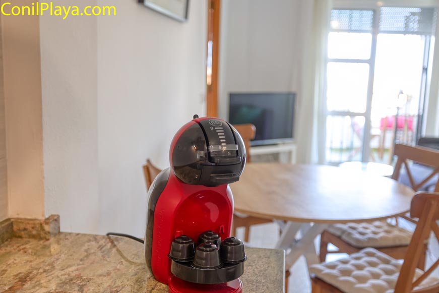 Cafetera de cápsulas roja sobre encimera y mesa redonda al fondo