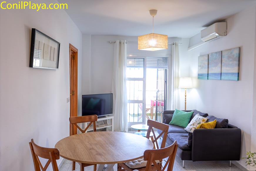 Salón con sofá mesa redonda y televisor junto a una ventana grande