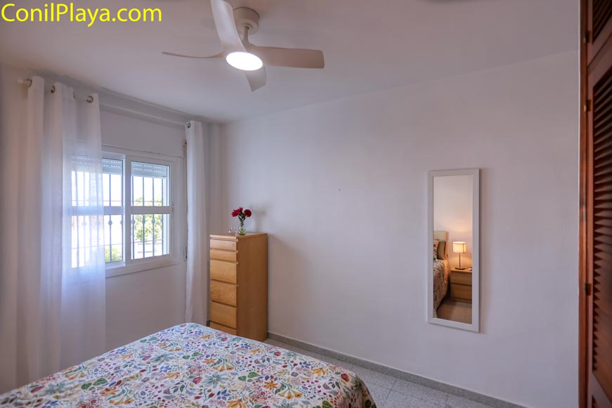Dormitorio con ventana, cama, cómoda y espejo en la pared